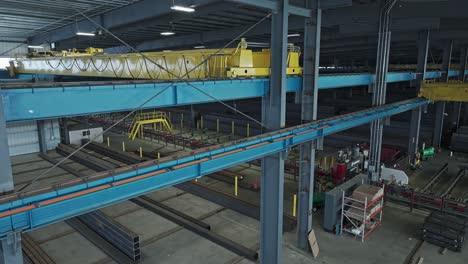 aerial descend inside of steel pipe beam warehouse establishes yellow overhead bridge crane