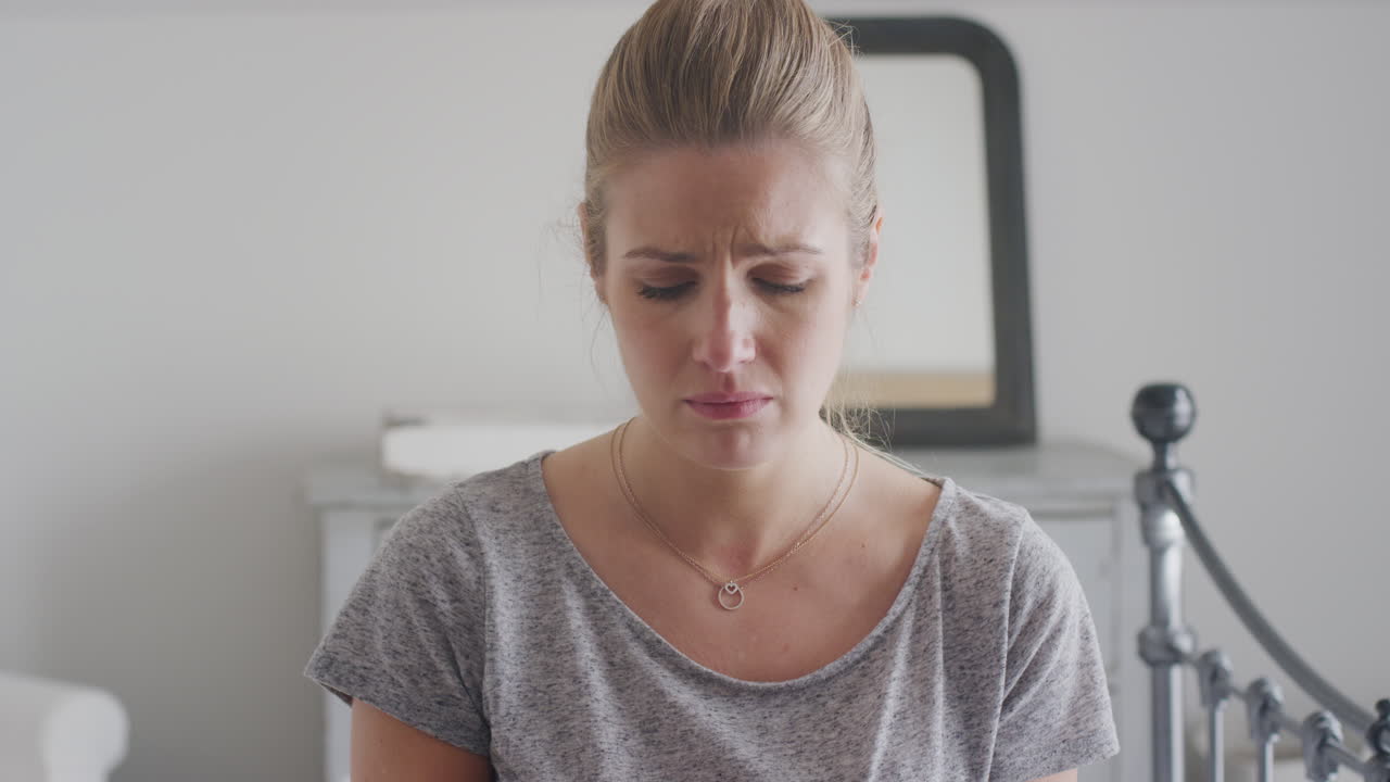 Unhappy Woman Wearing Pyjamas Sitting On Bed With Mobile Phone Being Bullied Online Via Social Media