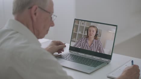 people is working remotely, communicating by video call, aged man is making notes and young woman is talking