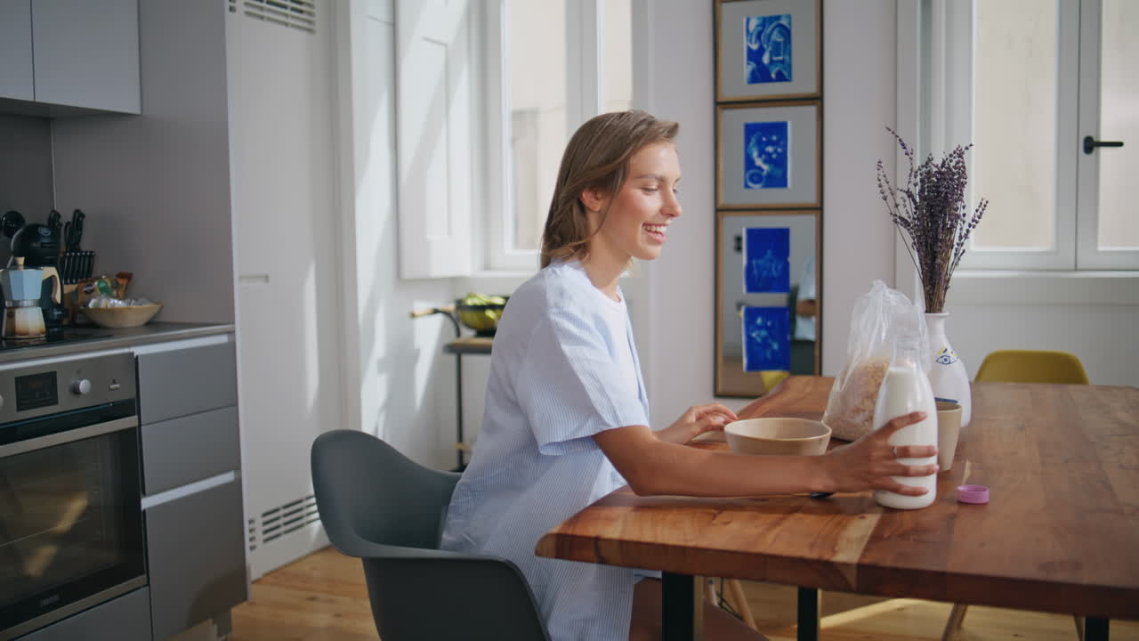 Breakfasting woman pouring milk into sweet cereal bowl. Relaxed lady sit table