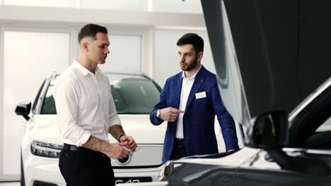 agent talking to a client standing near open hood of a car