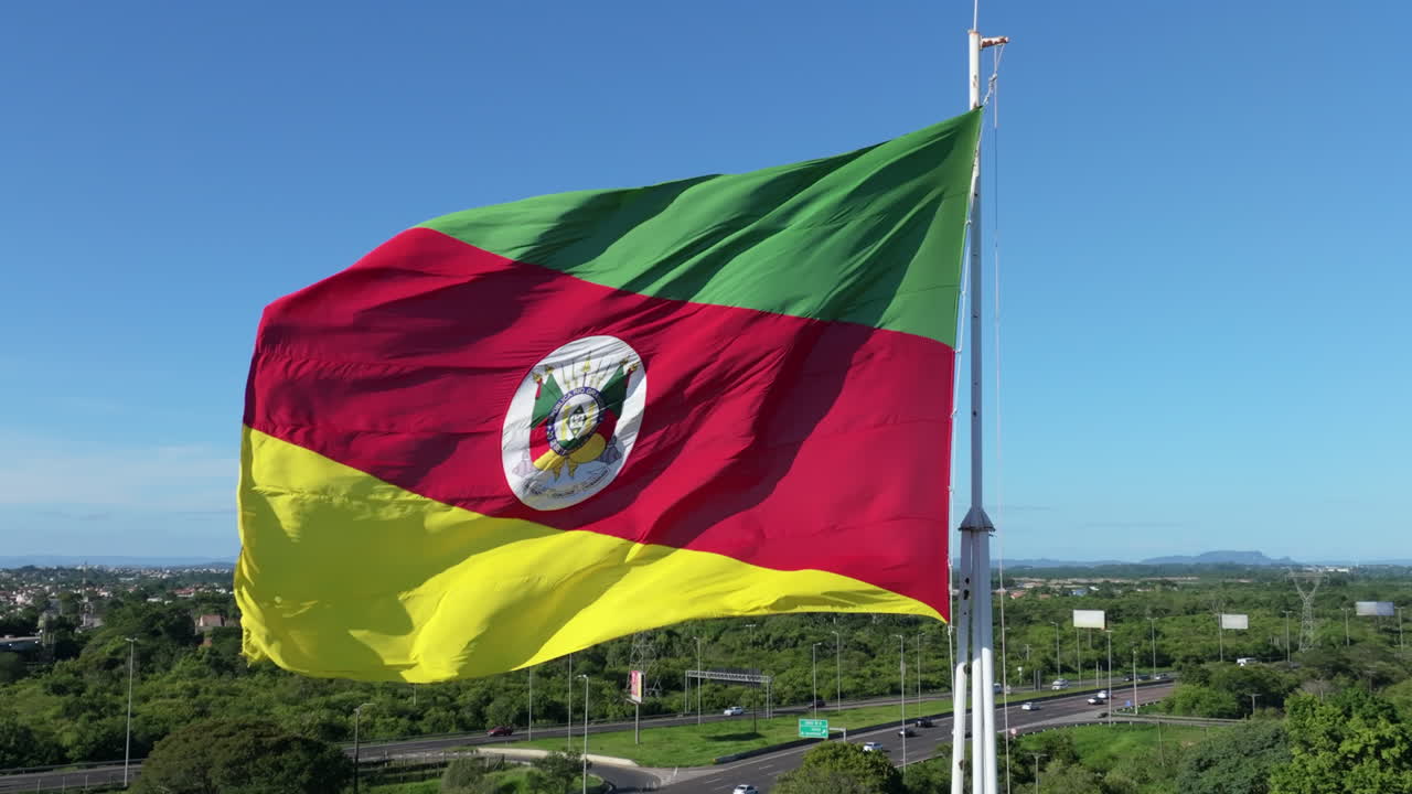 Bandiera del Rio Grande do Sul che sventola al rallentatore su un'asta alta sopra la città e l'autostrada sotto un cielo azzurro e limpido.