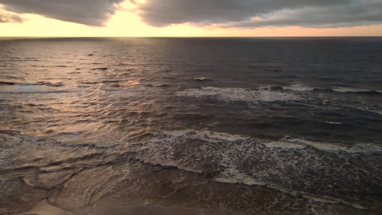 Ripresa aerea di un bellissimo tramonto sopra le onde oceaniche che si infrangono su una spiaggia sabbiosa
