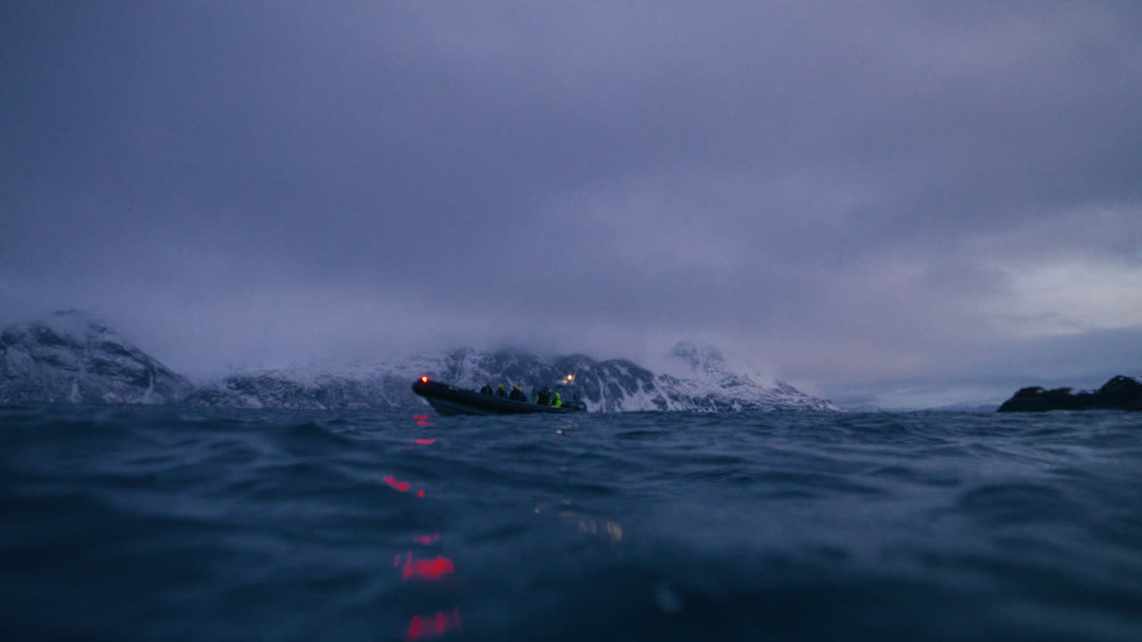 夕暮れの北極海に浮かぶ調査船。荒波の向こうには雪をかぶったノルウェーの山々が見える。