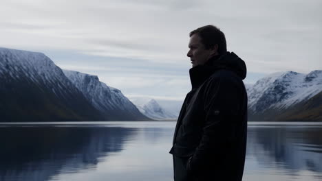 man looking out over a tranquil fjord surrounded by snow-capped mountains