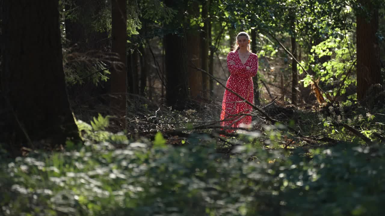 Una donna in abito rosso sta in piedi in una radura illuminata dal sole nella foresta oscura