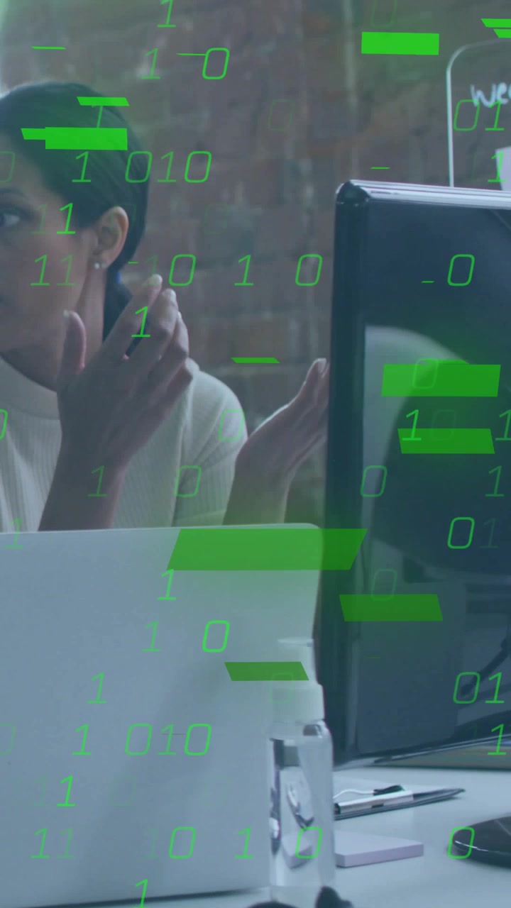 Vertical video: Woman talking at desk, computer causing binary code obscuring view for tech demo