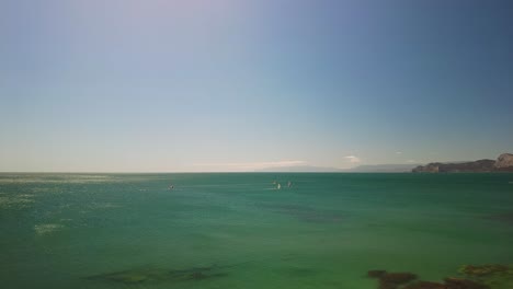 Crimea,-Cape-Megan,-surfers-with-a-sail-cut-through-the-green-water-of-the-Black-Sea-in-warm-spring-4k