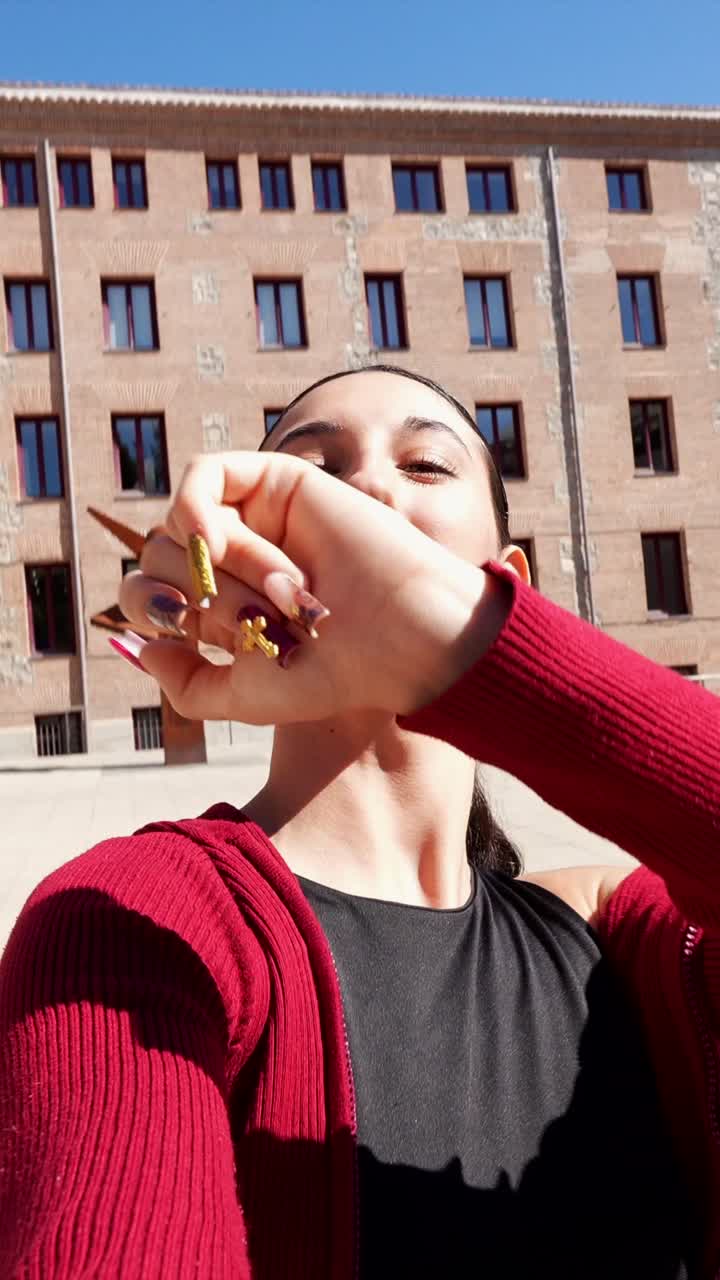 A woman poses outdoors with a brick building in the background
