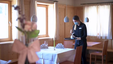 Waitress-with-face-mask-prepares-a-restaurant-table-with-wine-glasses