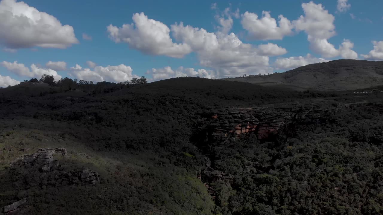 Iconic rock plateau formation in the Andorinhas park near Ouro Preto in Minas Gerais, Brazil, in shadow against a blue sky with clouds. Aerial backwards movement.