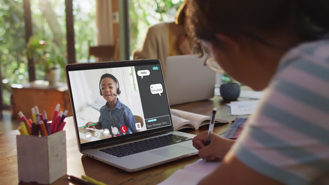 Schoolgirl using laptop for online lesson at home, with boy talking and web chat on screen
