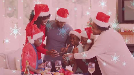 animation of snow falling over smiling family with santa hats using smartphone
