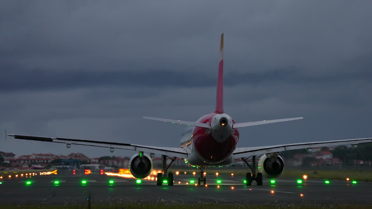Airplane positioned on runway during twilight, with bright lights illuminating the path ahead, creating a dramatic travel atmosphere