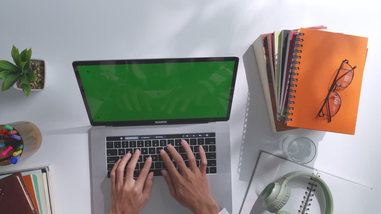 vista de arriba hacia abajo de una computadora portátil con pantalla verde simulada pantalla chromakey en un escritorio de oficina de madera al lado de la libreta con bolígrafos, gafas y un vaso de agua.