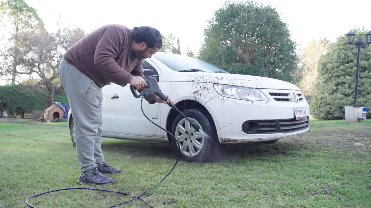 Homem lavando carro branco sujo com lavadora de alta pressão em um gramado