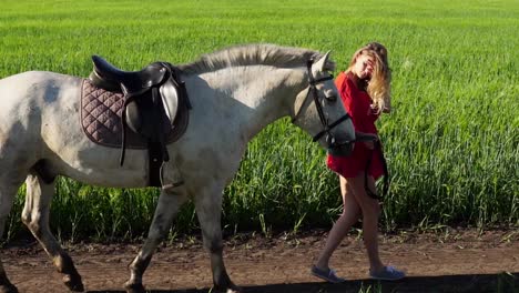 mujer caminando al lado de un caballo blanco en un campo