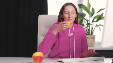 young woman drinking an healthy orange juice while using desktop computer at office