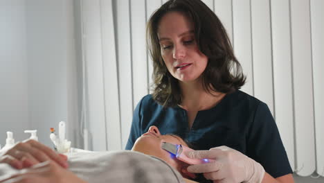 close up of practitioner using handheld ultrasound massage tool to gently massage customer face in bright spa room for professional skin care session and soothing wellness therapy showing expertise