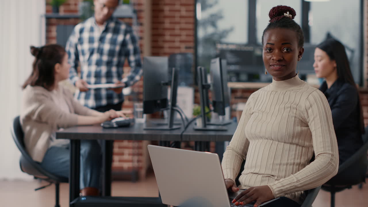 Portrait of african american coder sitting down writing programming language on laptop looking up and smiling