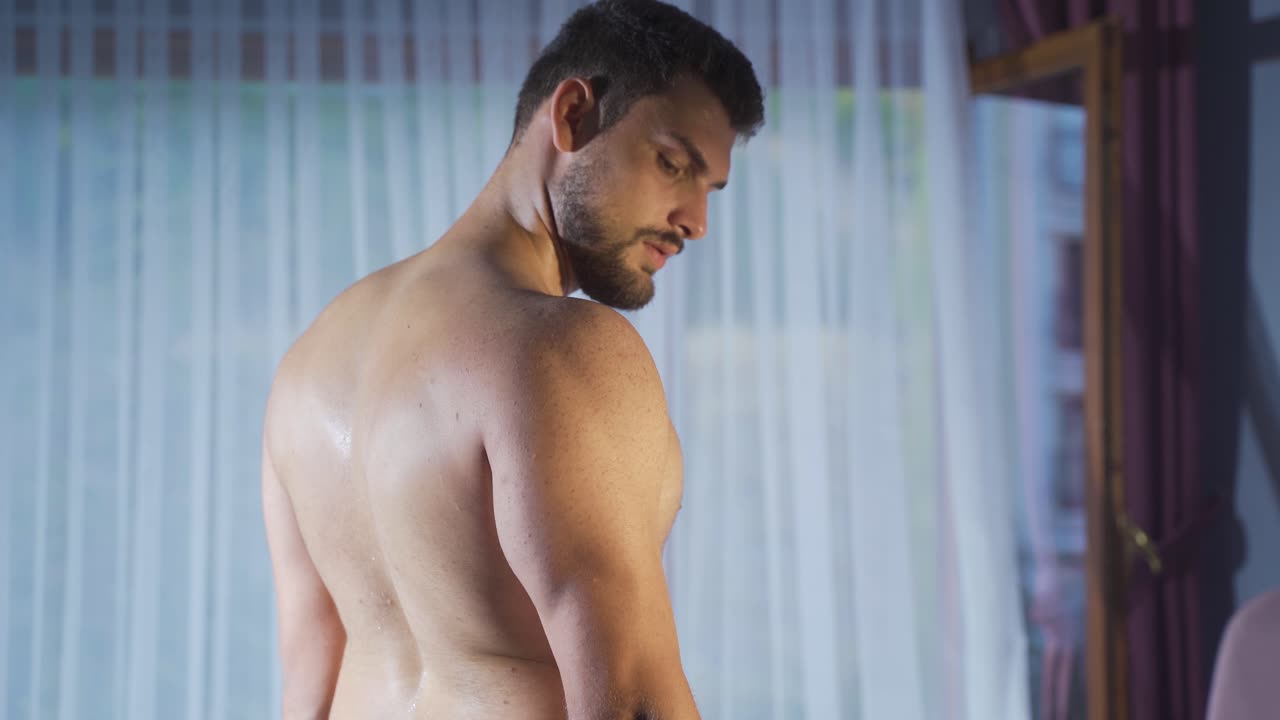 un musculoso culturista levantando pesas negras de pie en casa en cámara lenta.