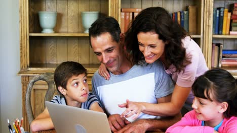 padres y niños usando computadora portátil en la mesa en la sala de estudio