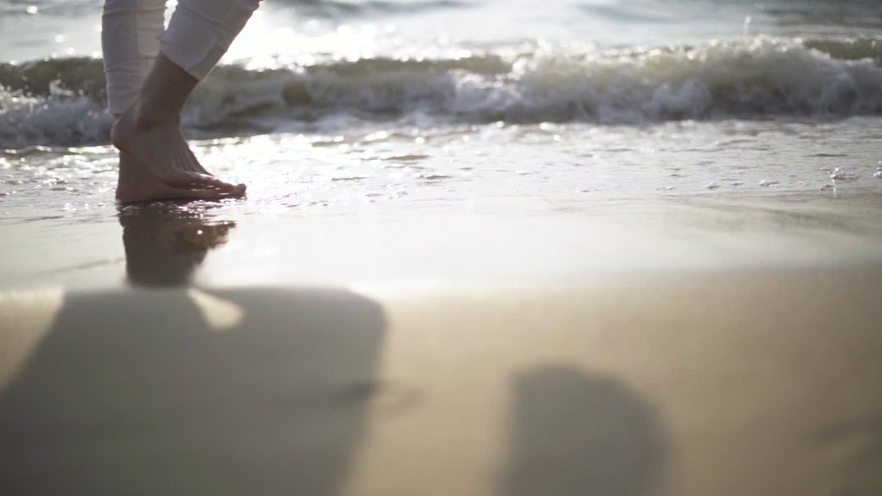 LOW ANGLE .Man walking barefoot by the beach while the sun sets.Waves at sunset.slow motion.Slow motion