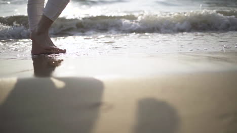 low angle .man walking barefoot by the beach while the sun sets.waves at sunset.slow motion.slow motion