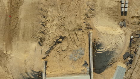 Vista-Aérea-De-Un-Sitio-De-Construcción-Con-Trabajadores,-Equipos-Y-Materiales-Sobre-Una-Superficie-De-Concreto,-Adyacente-A-Un-área-Excavada.