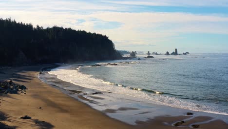 stunning descending aerial drone shot of the gorgeous third beach in forks, washington with large rock formations, cliffs, small waves and golden sand on a warm sunny summer morning