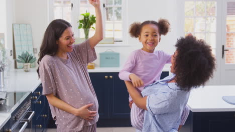 pregnant family with two mums dancing making morning pancakes in kitchen with daughter