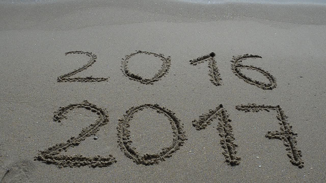 Shooting on the beach. New Year 2017 is coming concept - inscription 2016 and 2017 on a beach sand, the wave is almost covering the digits 2016