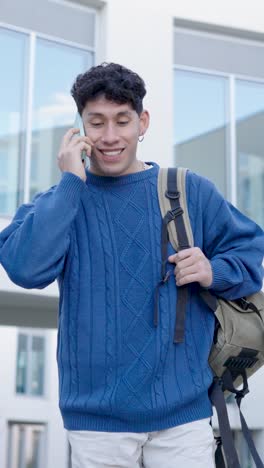 young latino student talking on phone while walking. vertical