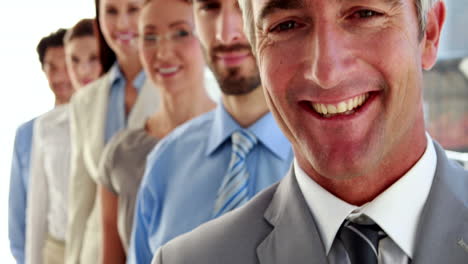 Business-team-standing-in-a-row-smiling-at-camera