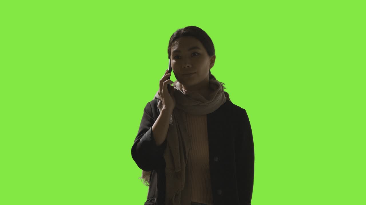 Scatto in studio a bassa chiave di donna frustrata che risponde a una chiamata sul cellulare, su sfondo verde.