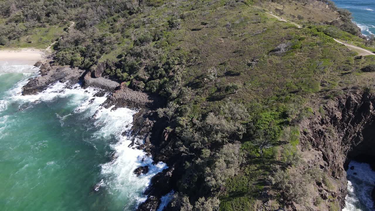 Aerial drone pans down over Noosa park with beach views on a bright sunny day