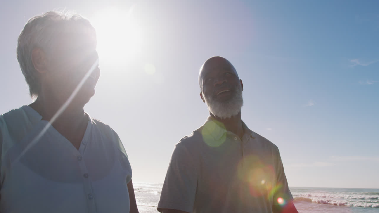 미소 짓는 아프리카계 미국인 부부가 해변에서 손을 잡고 고 있습니다.