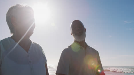 una pareja de adultos africanos-americanos sonrientes caminando y tomados de la mano en la playa