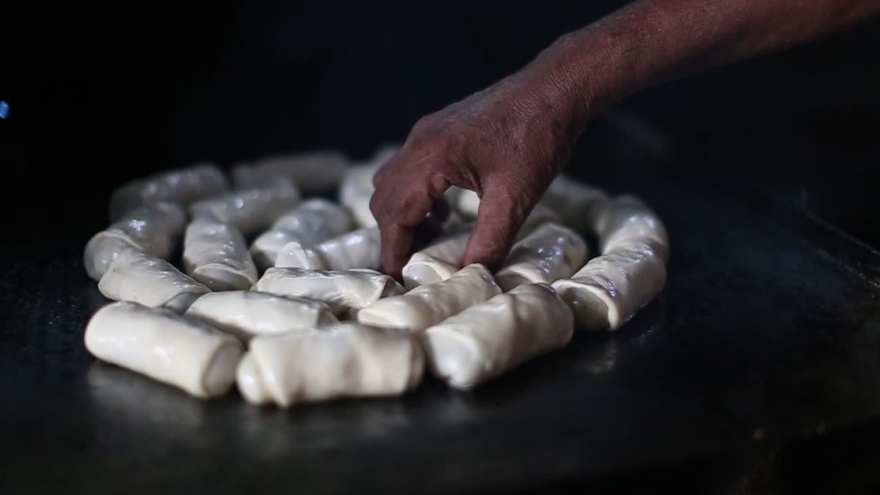 Hand reaches into a group of rolls being cooked on a griddle