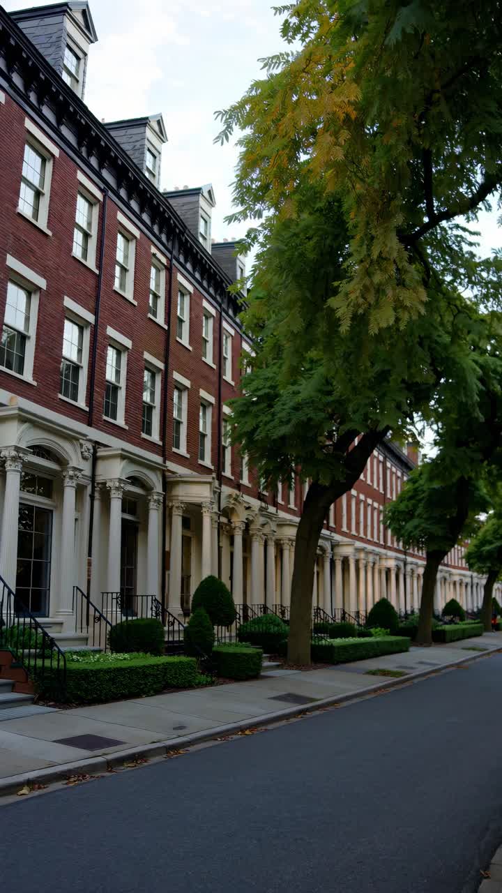 Street-level video view of elegant red-brick townhouses with lush trees lining the sidewalk