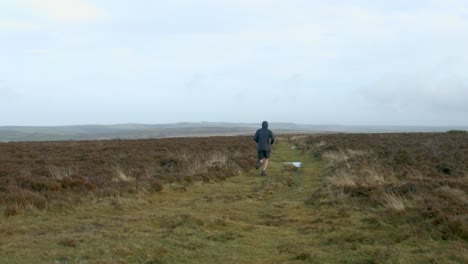 male marathon athlete running away from camera on a training run over exmoor uk 4k