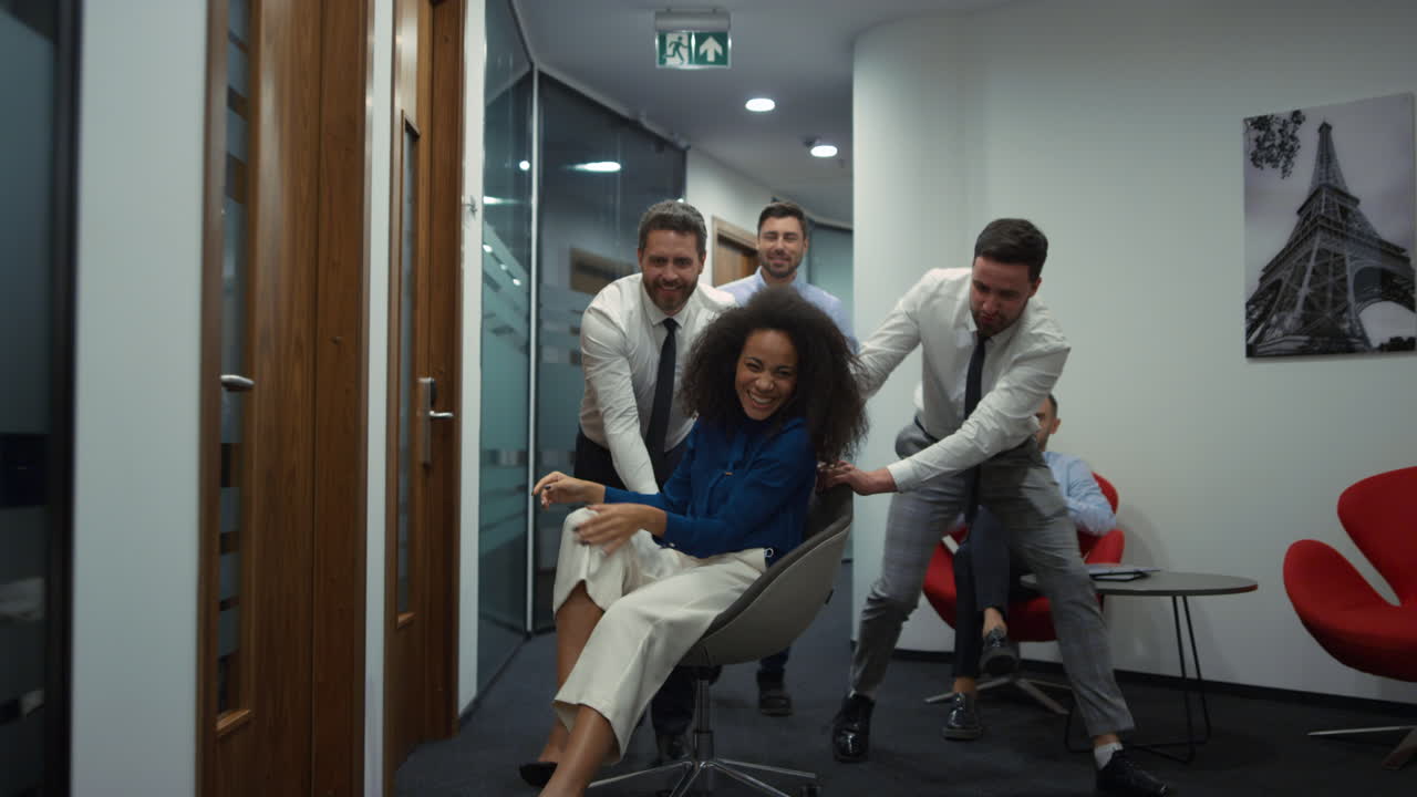 Business group racing chair having fun party in diverse office workplace hallway