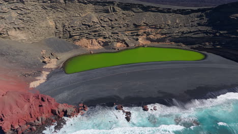 green lagoon known as charco de los clicos, surrounded by black sand beach and red cliffs on the volcanic island of lanzarote