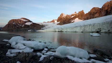 Peaceful-morning-scene-at-the-glacial-lake-next-to-Claridenfirn-glacier-in-Uri,-Swizerland-with-the-alpenglow-of-the-alpine-peaks-reflected-and-icebergs-on-shore