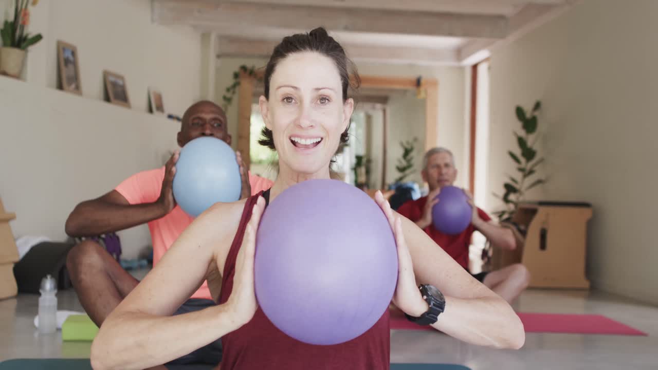 Diverse seniors holding balls exercising with female pilates coach, unaltered, in slow motion