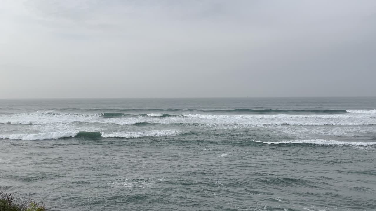 Soft waves gently lap against the Portuguese coastline, stretching out under a hazy sky. The tranquil seascape offers a serene view of the ocean meeting the horizon in a peaceful beach setting.