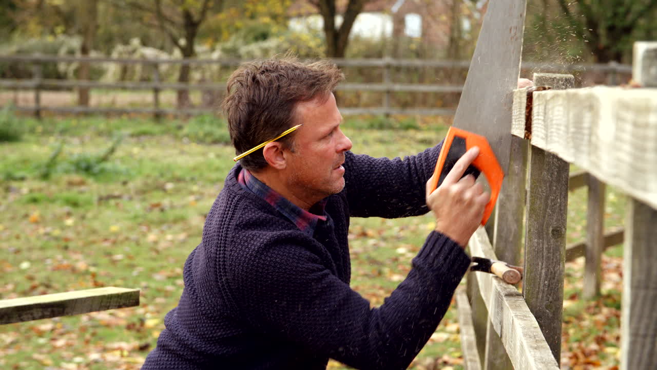 hombre maduro arreglando la valla al aire libre con sierra