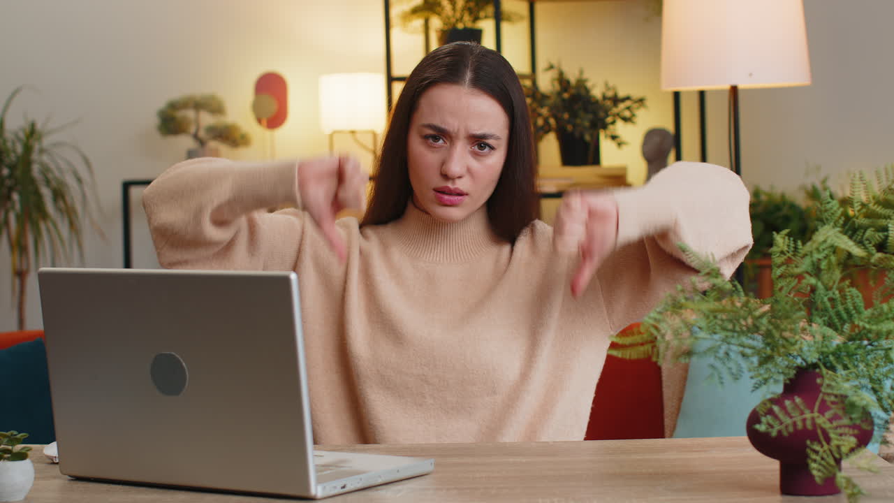 Upset caucasian woman showing thumbs down dislike bad work disapproval dissatisfied feedback at home