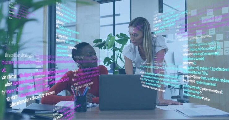 Software engineer typing code with overlay, coworker approaching reviewing notebook for review