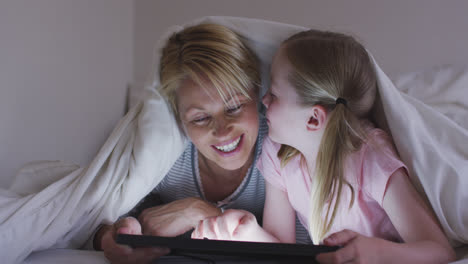 vista frontal de una mujer caucásica y su hija usando una tableta digital en la cama